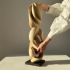 Hand holding the Convergence walnut sculpture to show its size and handcrafted details.