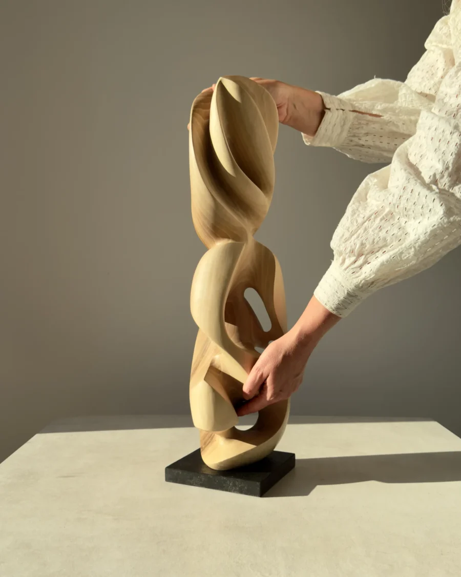 Hand holding the Convergence walnut sculpture to show its size and handcrafted details.