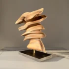 Front view of Fluens, a one-of-a-kind abstract walnut sculpture with flowing layered forms on a black wooden base.