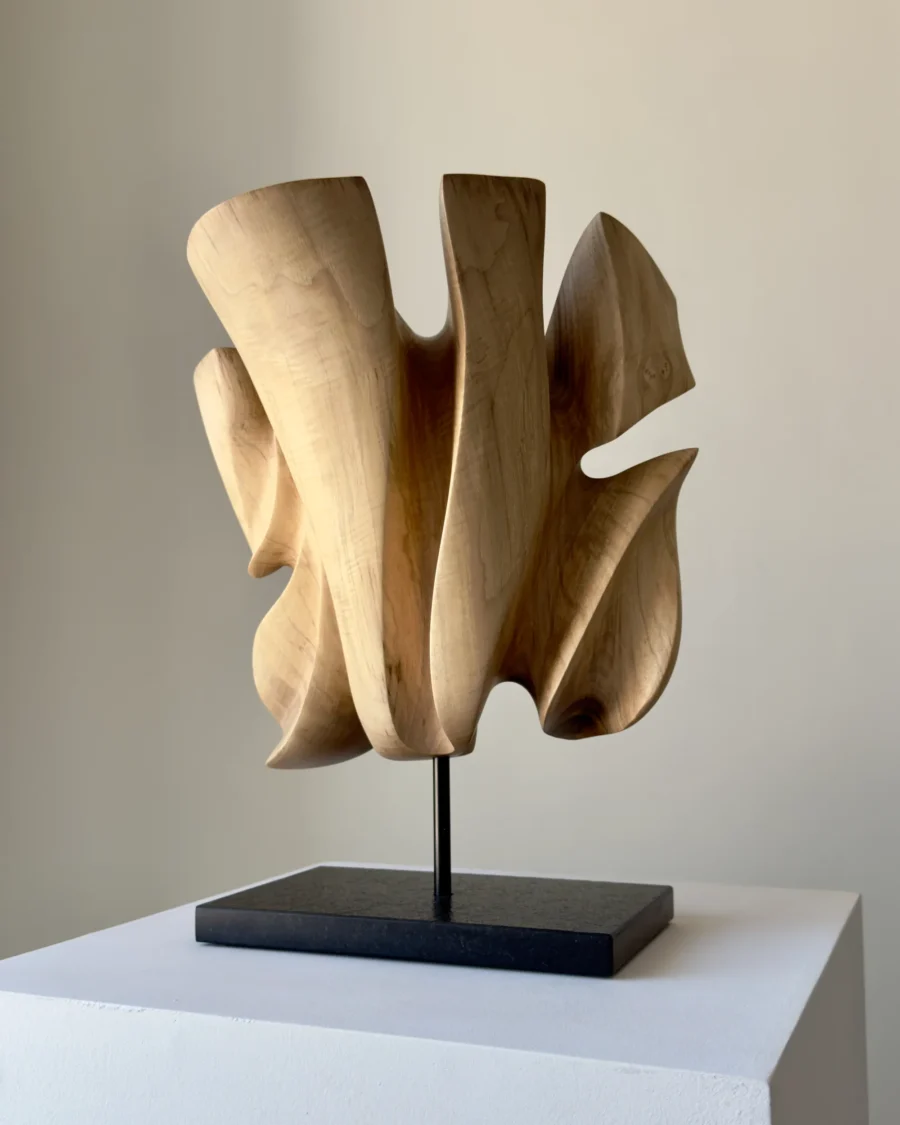 Left-side view of Folded Presence abstract walnut sculpture on a polished black granite base.