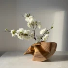 Hand-carved abstract walnut sculpture displayed as a sculptural vase with a flowering branch.
