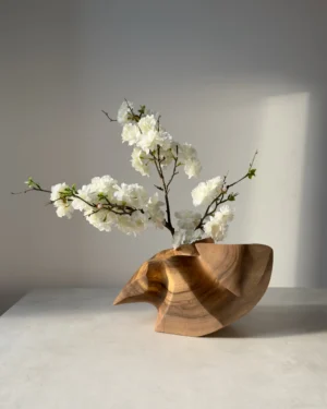 Hand-carved abstract walnut sculpture displayed as a sculptural vase with a flowering branch.