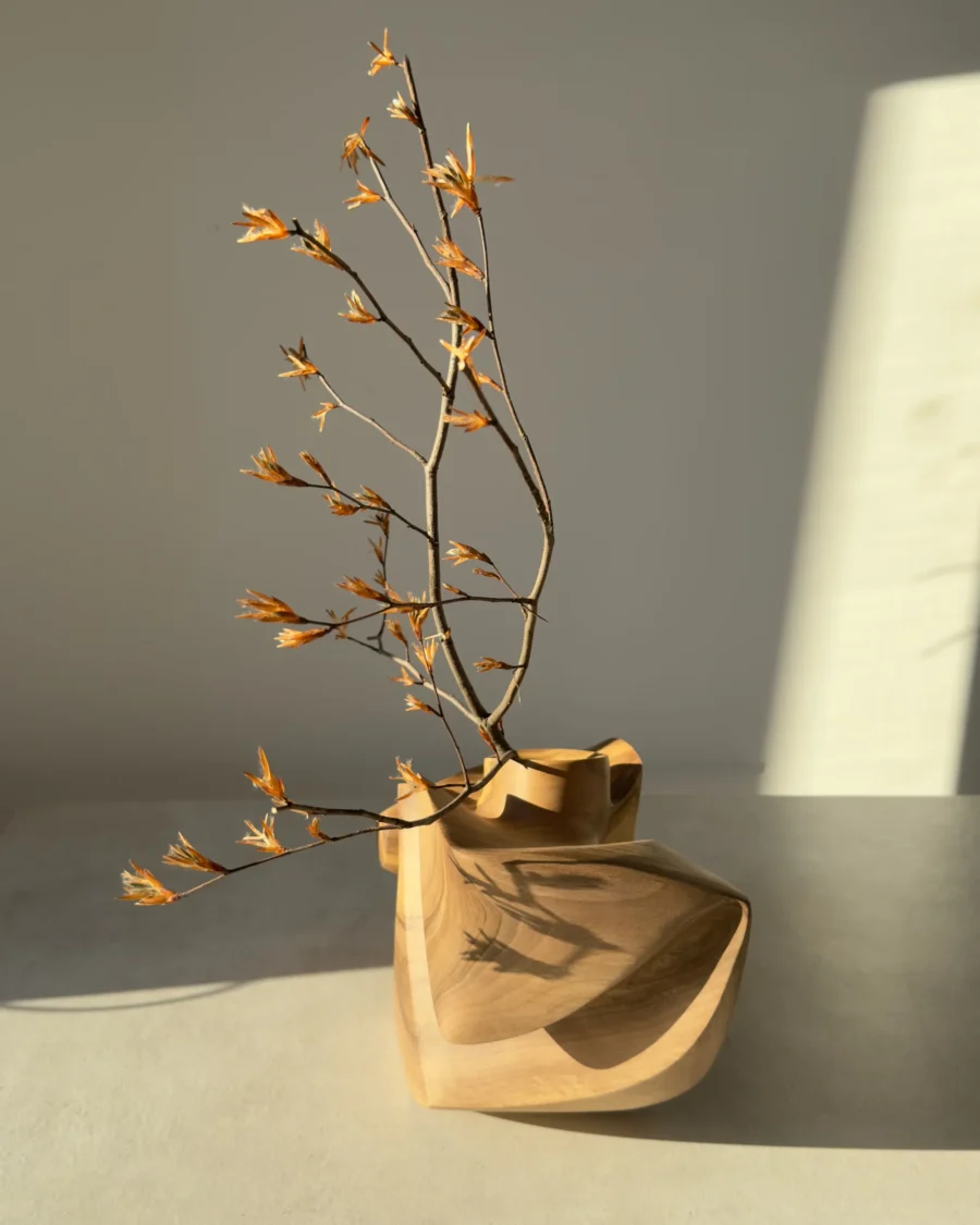 Abstract walnut wood sculpture with a sculptural opening holding a delicate flowering branch.