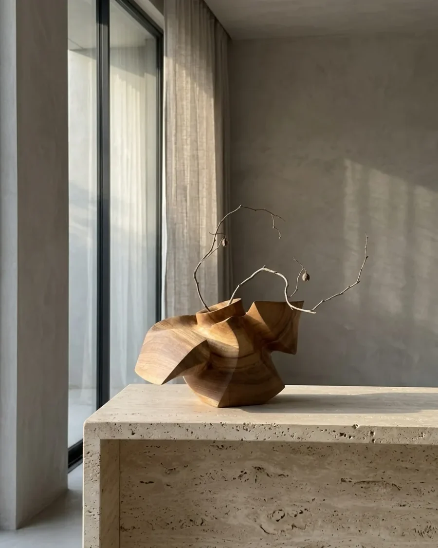 Sculptural walnut vase displayed in a contemporary interior with a flowering branch.