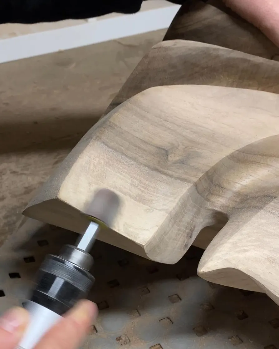 Carefully sanding a hand-carved walnut sculpture to refine its flowing surfaces.