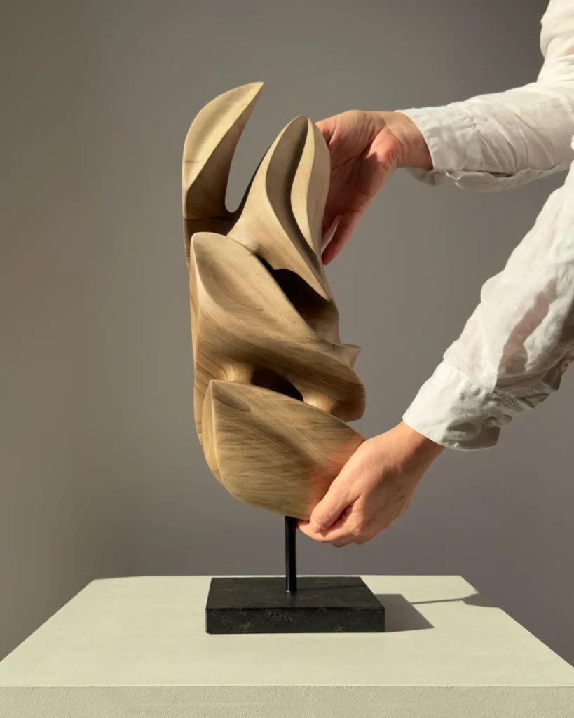 Silent Ascent walnut wood sculpture shown with a hand for size reference.