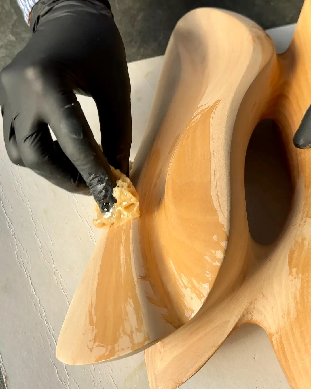 Final oil application on the hand-carved Sway sculpture before completion.