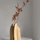 Twin Presence sculptural walnut vase displayed with a single natural branch in its removable glass insert.