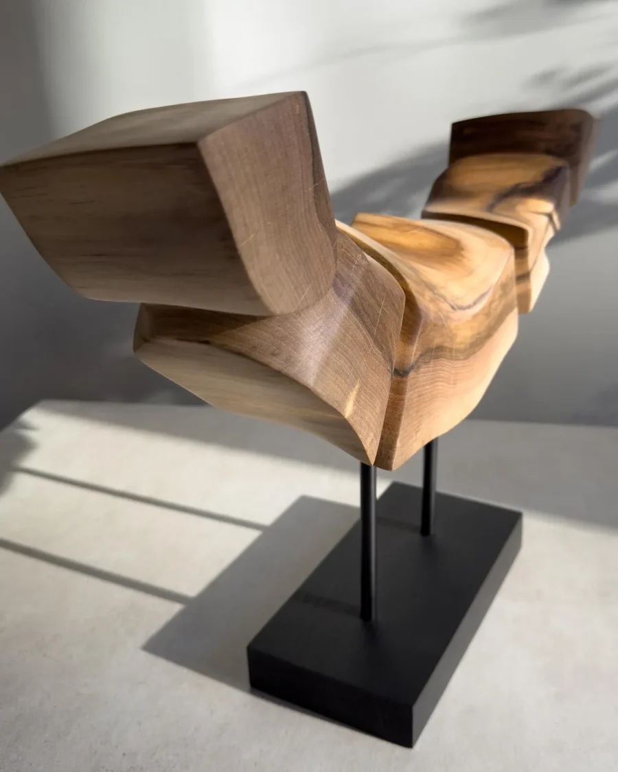 Dynamic Contours one-of-a-kind abstract walnut sculpture with a horizontal carved form raised on steel supports above a black base.