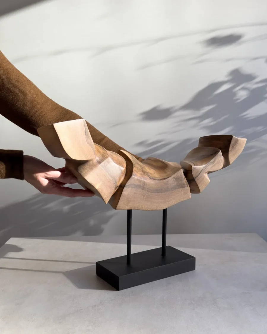 Dynamic Contours hand-carved walnut sculpture shown with the artist’s hands for scale, suspended above a black wooden base.