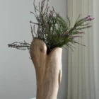 Hollow sculptural walnut vase with white dried flowers, showing the smooth exterior grain and irregular dark opening