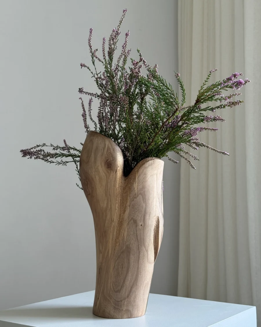 Hollow sculptural walnut vase with white dried flowers, showing the smooth exterior grain and irregular dark opening
