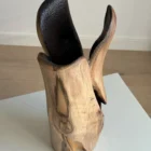 Hollow sculptural walnut vase from the side, revealing a large dark opening beneath a smooth curved section of wood.