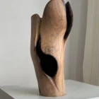 Hollow organic modern walnut vase displayed as a sculpture, with layered carved forms and a narrow shadowed opening.
