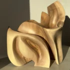 Unfurl abstract walnut sculpture in warm natural sunlight, revealing curved surfaces, deep shadows and contrasting walnut grain.