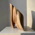 Unfurl abstract walnut sculpture displayed on a white pedestal, showing its layered hand-carved form and natural wood grain