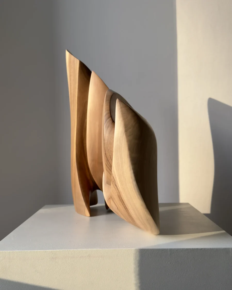 Unfurl abstract walnut sculpture displayed on a white pedestal, showing its layered hand-carved form and natural wood grain