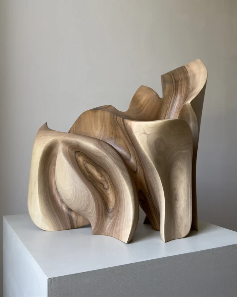 Front view of Unfurl walnut sculpture in natural light, revealing the rhythm of its upright carved planes and smooth walnut surfaces.