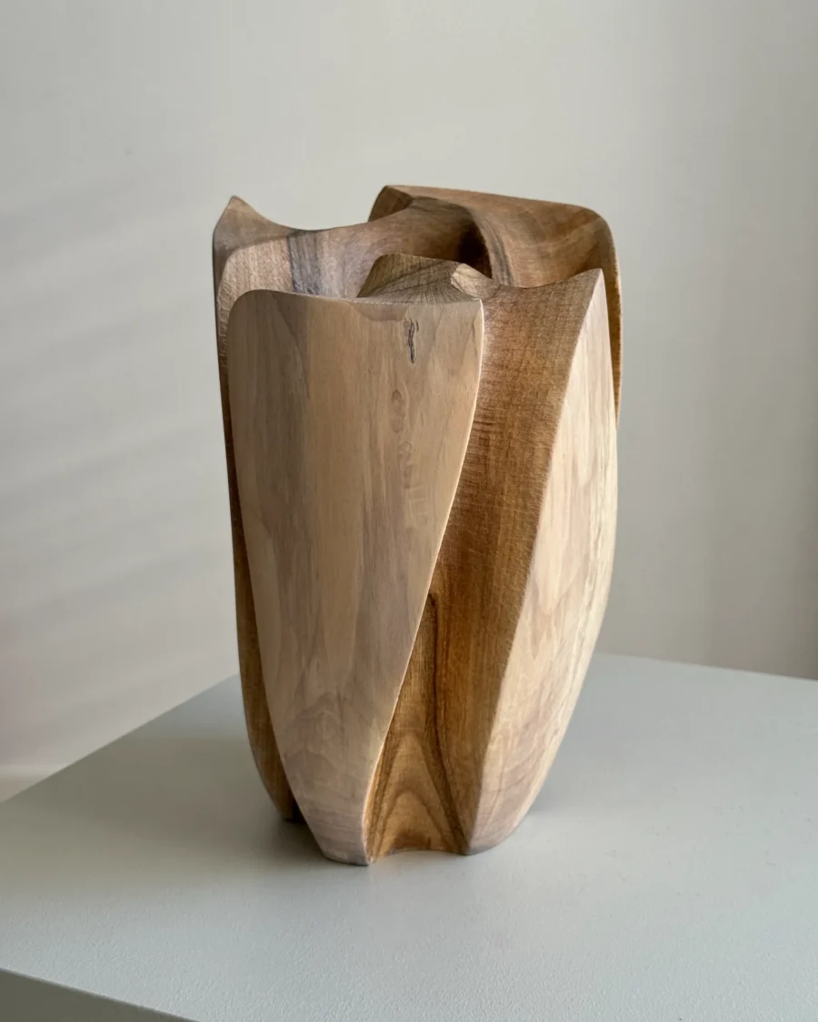 Angled view of Within highlighting its layered construction, curved walnut planes and changing light across the carved edges.