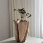 Front view of Within holding a single dried flower, with pale walnut surfaces and darker carved channels visible below.