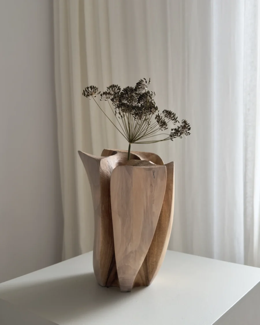 Front view of Within holding a single dried flower, with pale walnut surfaces and darker carved channels visible below.