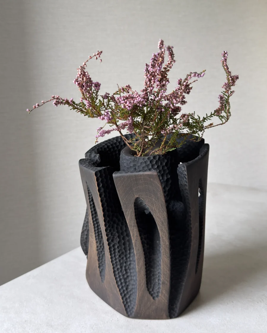 Construct applewood vessel with heather arrangement, photographed in natural light from a slightly elevated angle.