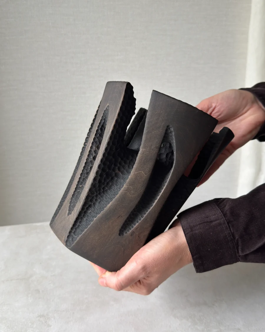 Side view of Construct held in two hands, showing the dark applewood finish, carved openings and sculptural scale.