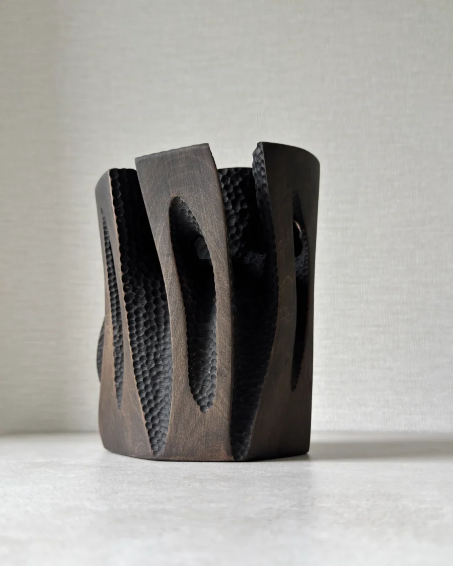 Construct modern wood vase showing layered carved panels, dark textured surfaces and visible applewood grain.