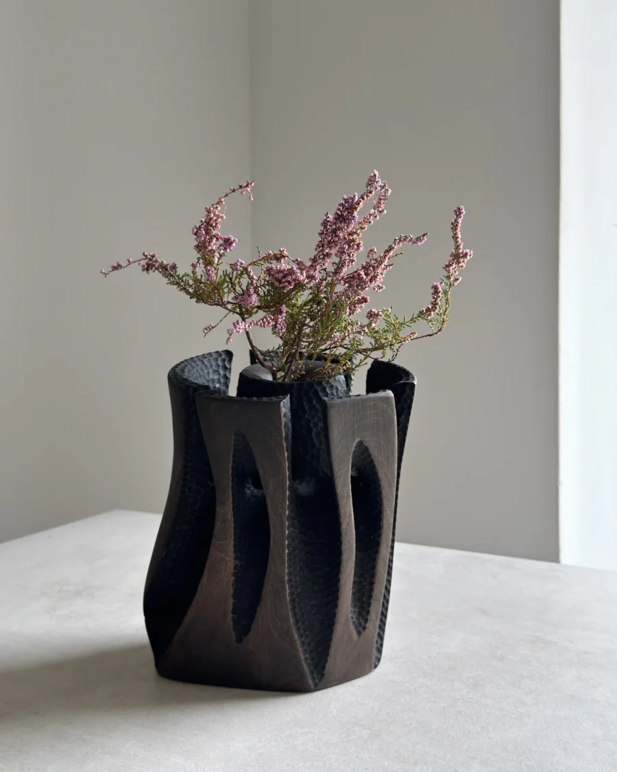 Dark hand-carved applewood vase with heather branches, showing the contrast between smooth outer planes and textured recesses.
