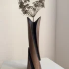 Tall sculptural cherry wood vase with delicate dried flowers, showing how botanical stems continue the upward movement of the carved form.