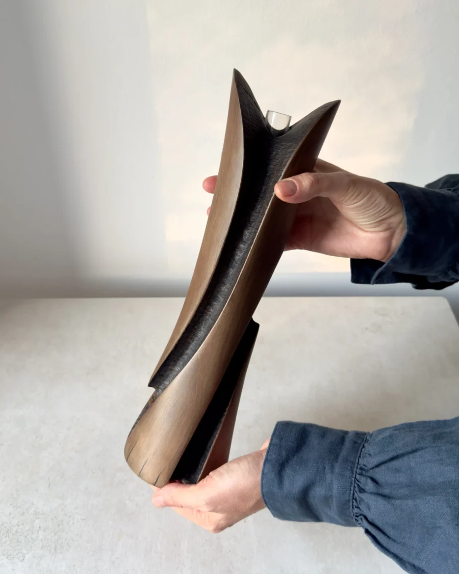 Emergence sculptural wooden vase held in two hands to show its 34 cm height, curved planes and dark recessed carving.