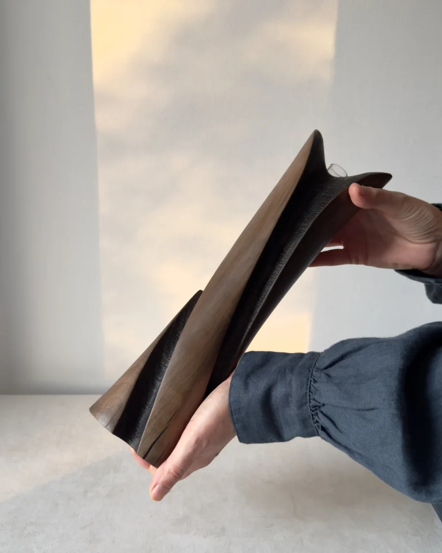 Emergence sculptural wooden vase held in two hands to show its 34 cm height, curved planes and dark recessed carving.