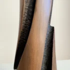 Detail of the sculptural cherry wood vase with a smooth elongated outer plane beside a deep hand-textured dark recess.
