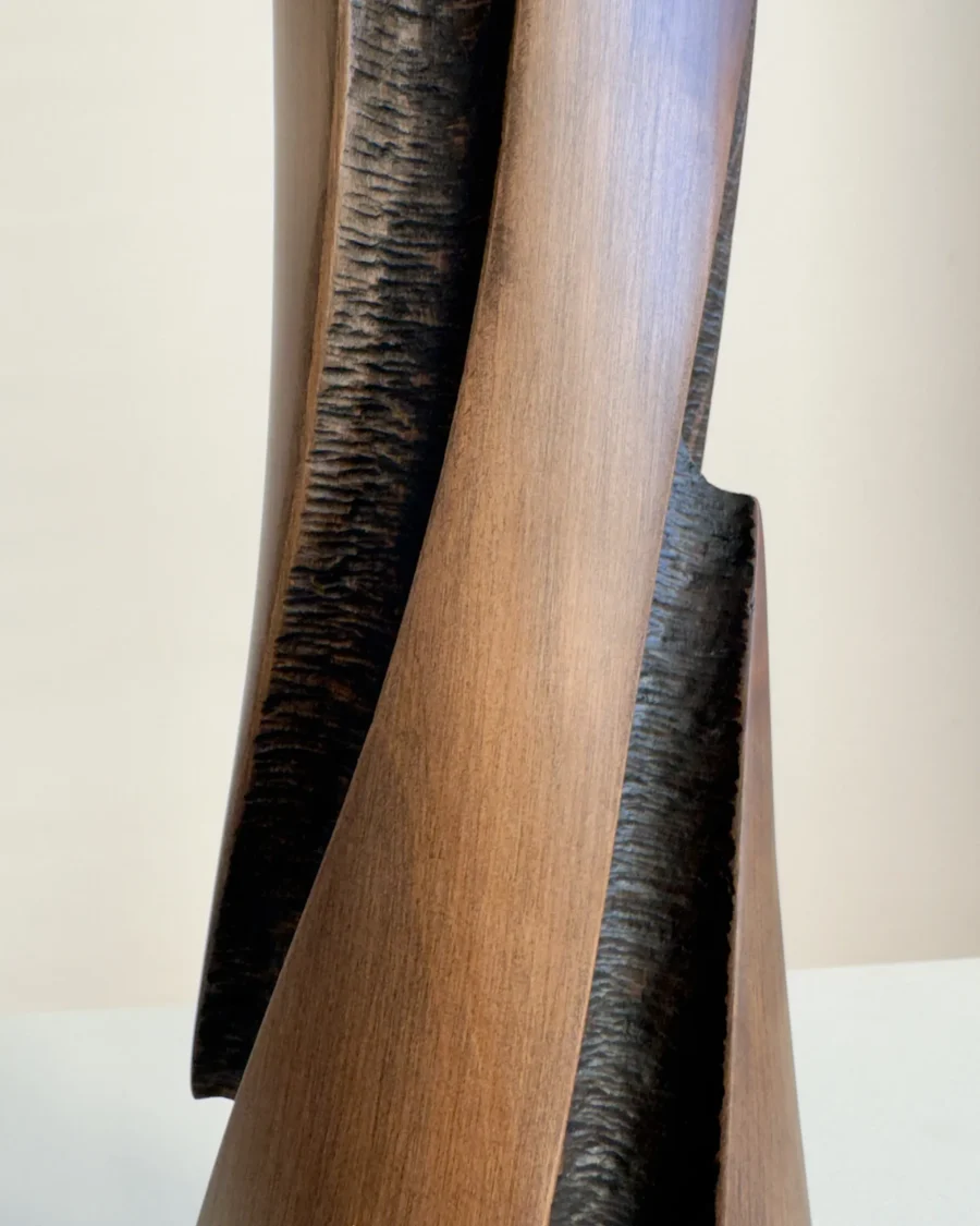 Detail of the sculptural cherry wood vase with a smooth elongated outer plane beside a deep hand-textured dark recess.