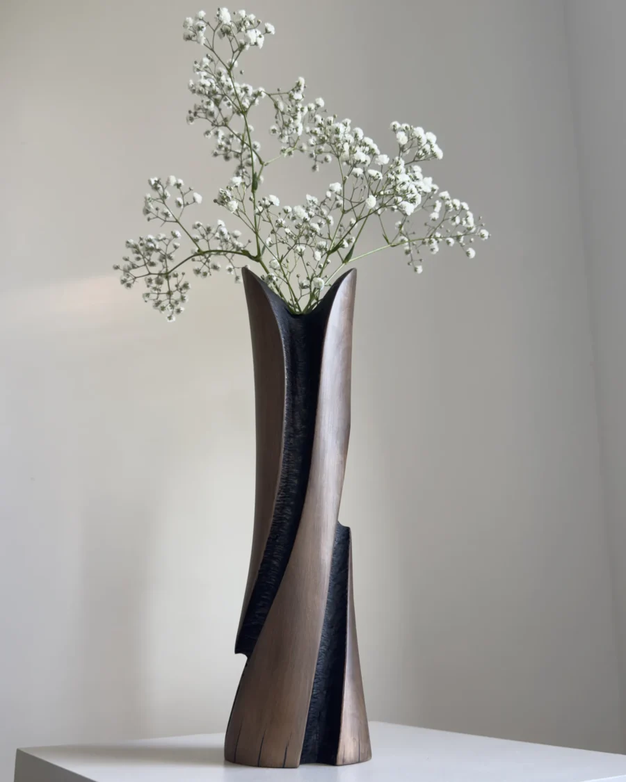 Sculptural cherry wood vase with white gypsophila arranged in the glass insert, showing the contrast between warm brown wood and dark texture.
