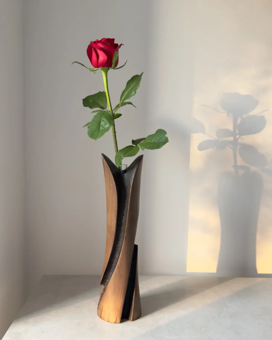 Hand-carved cherry wood bud vase with a fresh red rose in the removable glass tube, photographed in warm natural light.