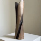 Emergence displayed without flowers in natural light, showing its warm brown cherry wood surface, dark carved recess and asymmetrical top.