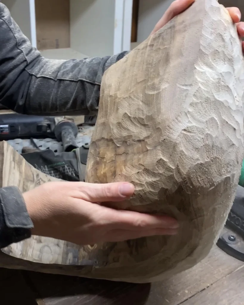 Ewelina Głowacz holding a hand-carved raw wood form in her sculpture studio in Poland