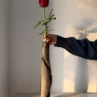 quiet-turn-walnut-sculptural-vase-single-rose Hand carved walnut sculptural vase Quiet Turn with a single red rose, shown in warm natural light with the artist’s hand for scale.
