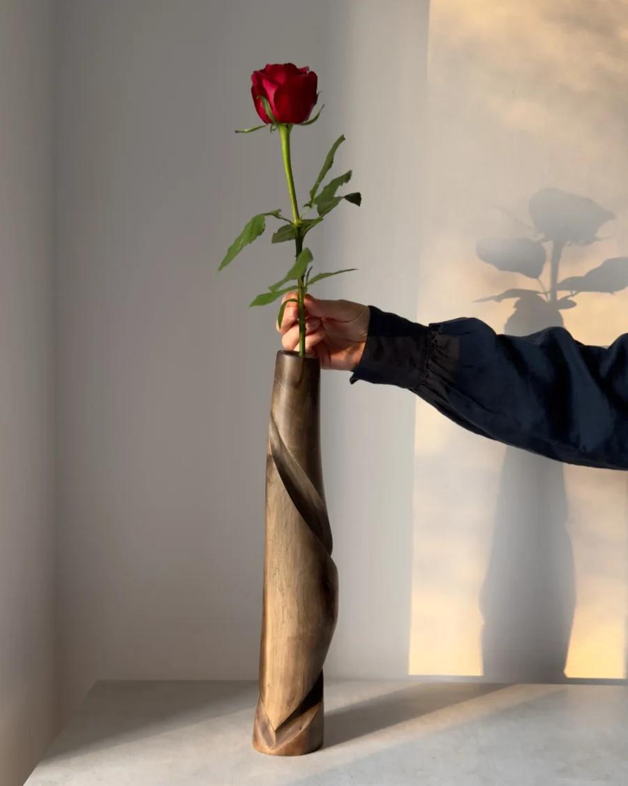 quiet-turn-walnut-sculptural-vase-single-rose Hand carved walnut sculptural vase Quiet Turn with a single red rose, shown in warm natural light with the artist’s hand for scale.